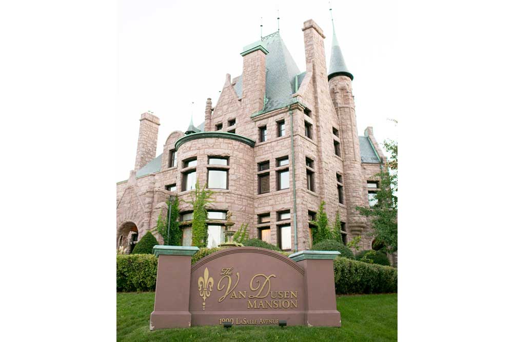 The Van Dusen Mansion is a red stone castle with cylindrical towers capped with green, pointed roofs. 