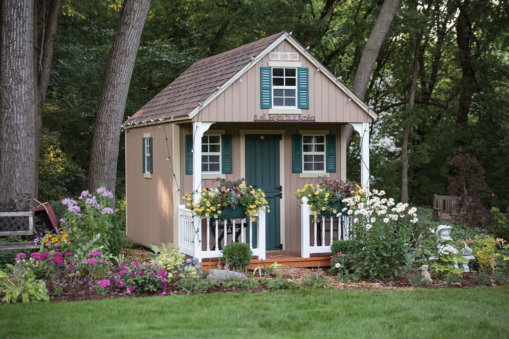 A quaint gardening shed with white railings and green shutters.
