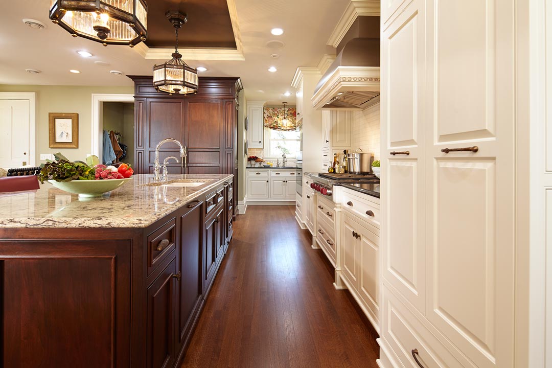 A kitchen with hardwood floors, white cabinetry and chandeliers hanging above the center island.