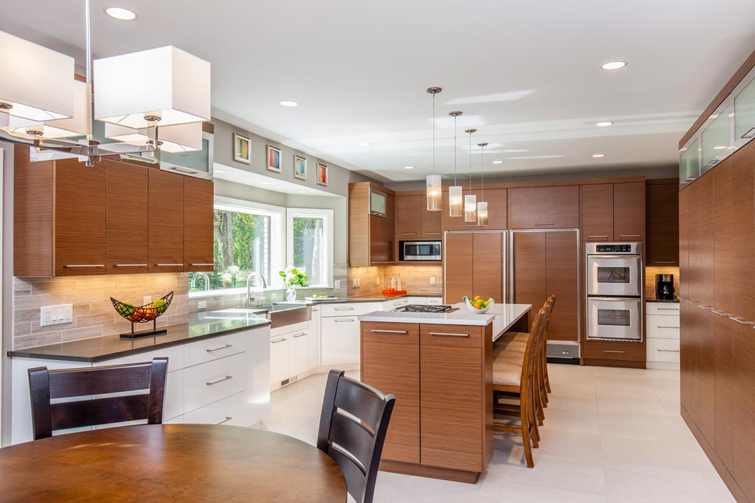 A kitchen featuring stainless steel appliances, white and brown cabinetry, and lights hanging above the center island.