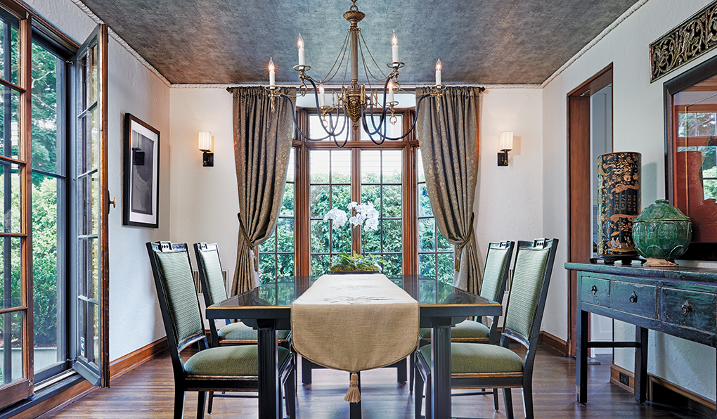 An elegant dining room shows windows surrounding a table and chairs set underneath an ornate chandelier.