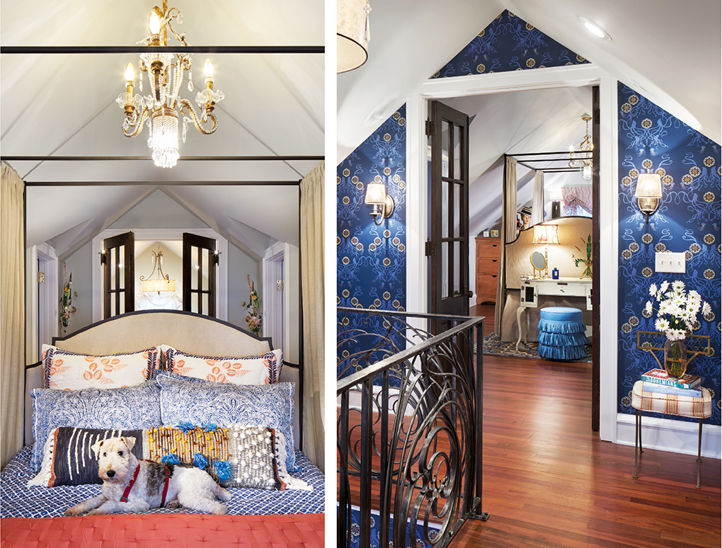 A master bedroom showing blue, patterned wallpaper, bedspread and pillows. A coral blanket and family dog rest on the bed underneath a chandelier.