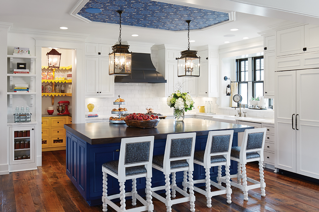 A white kitchen features a subway tile backsplash, blue island and blue wallpaper overhead.