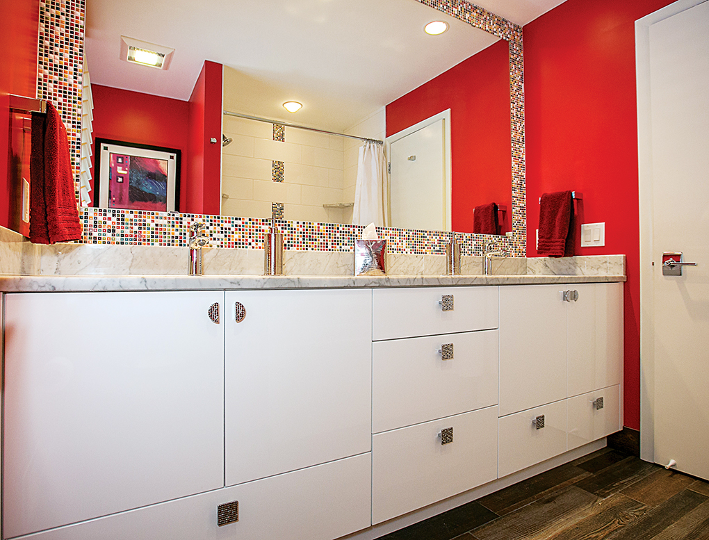 A bathroom featuring red walls, wood-plank floor tile, colorful mosaic tiles above the vanity and marble countertops.