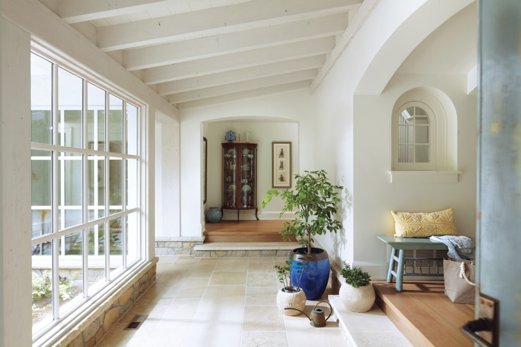 A remodeled home by Albertsson Hansen Architecture features a raftered ceiling, tile floor and large windows.