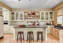 A kitchen designed by Gigi Digiacomo of Digiacomo Homes, Inc. shows light-colored hardwood flooring, white cabinetry, black countertops and an island surrounded by dark-colored wooden stools.