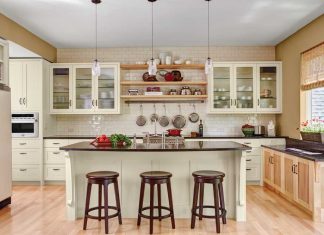 Digiacomo Homes, Inc. A kitchen designed by Gigi Digiacomo of Digiacomo Homes, Inc. shows light-colored hardwood flooring, white cabinetry, black countertops and an island surrounded by dark-colored wooden stools.