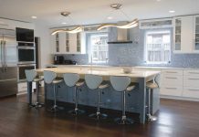A kitchen designed by Nicole Sirek of Partners 4, Design on the 2017 ASID Kitchen Tour. White cabinetry is accented by a blue-tiled backsplash. In the center of the kitchen is a blue-colored island with a white countertop, and is surrounded by blue stools.