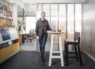 Jody McGuire stands next to white table with a model homes place on top of it in the middle of an office.