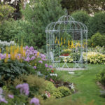 A Look Inside a Master Garden in Plymouth An open gazebo is surrounded by a lush garden full of green plants and colored flowers.