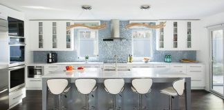 Jordana Green and Mark Grossfield Rebuild Their St. Louis Park Home A sleek and modern kitchen with white cabinetry, stainless steel appliances, and an ceiling-height opalescent tile backsplash.