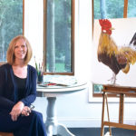 Artist Bonnie Folkerts Reinvents Herself A portrait of Bonnie Folkerts with a painting of a rooster next to her.