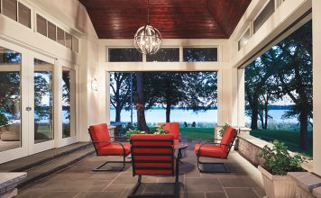 A semi-outdoor patio features a table and chairs, clerestory windows and large pocket doors with Phantom screens that look out onto a lake.