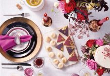 A table decorated with holiday gift ideas, including black plates and flatware, purple salad plates, deep-cut crystal goblets, white marble cheese plates, candles, flowers and more.