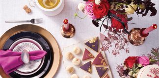 A table decorated with holiday gift ideas, including black plates and flatware, purple salad plates, deep-cut crystal goblets, white marble cheese plates, candles, flowers and more.