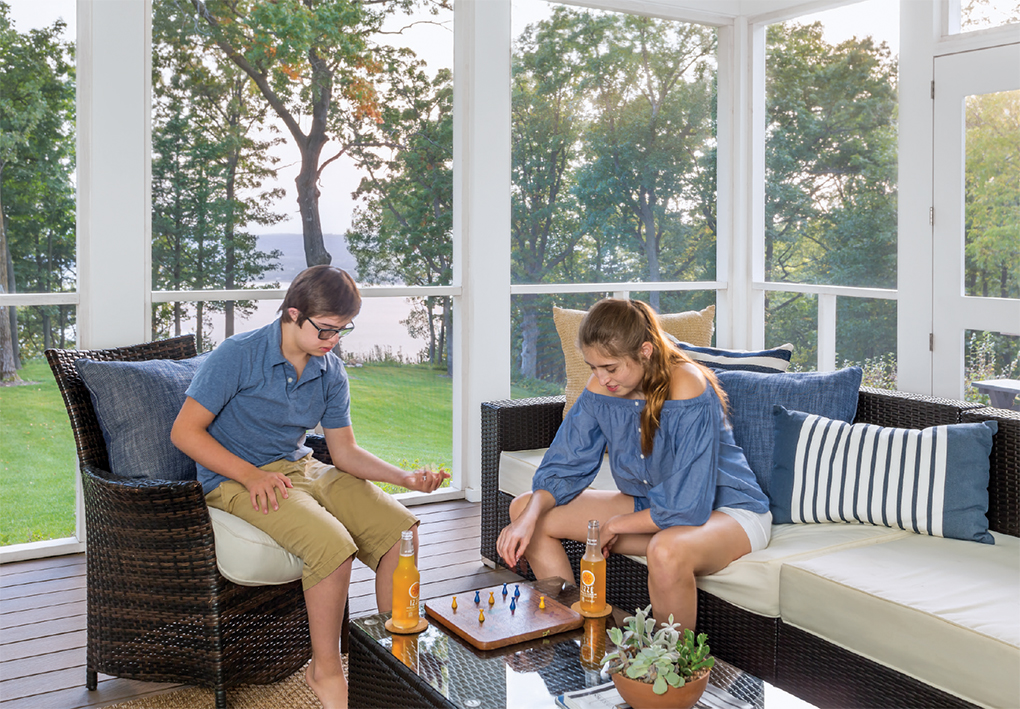 Two kids sit at a table in a screen porch playing a board game.