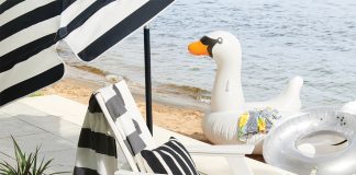 Outdoor Accessory Necessities A white deck chair with a tray of beverages and umbrella next to water.