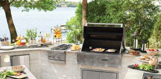 Lakeside Feast An outdoor kitchen with stainless steel grill, plates of food, and a table.