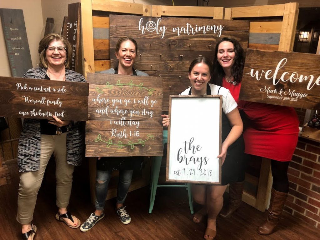 Group of women holding wood sign projects.