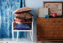 A room with decor influenced by the east features a blue rug, blue curtains, blue wall, chair, and table.