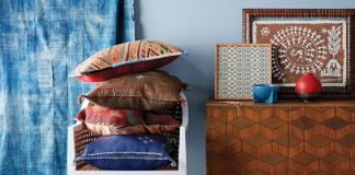 A room with decor influenced by the east features a blue rug, blue curtains, blue wall, chair, and table.