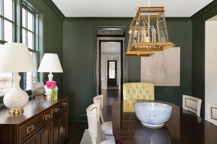 The dining room of a home on Midwest Home's 2018 Luxury Home Tour that features green walls, and a dark wood table with seating and chandeliers hanging overhead.