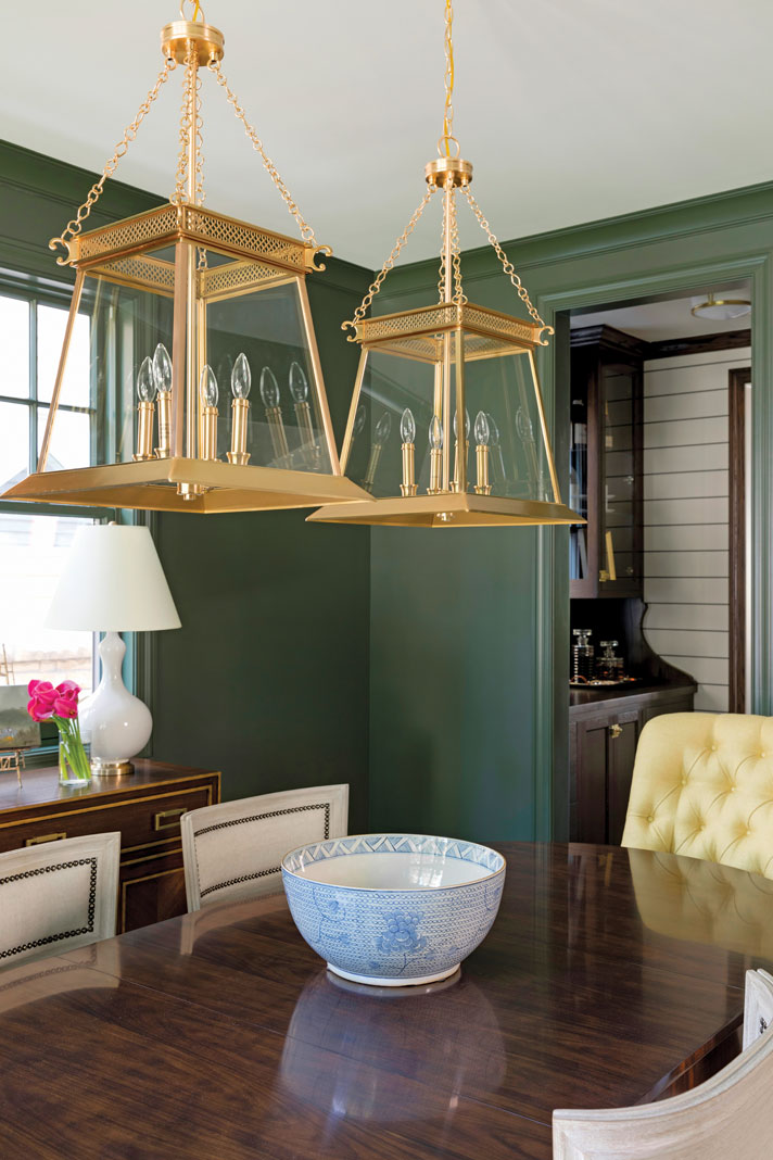 The stately dining room is a study in traditional elegance; a dark wood, glossy-finished oval table parallels the wood floors, while dark green walls and trim accentuate the room’s dramatic hanging lights. Part of Midwest Home's 2018 Luxury Home Tour.