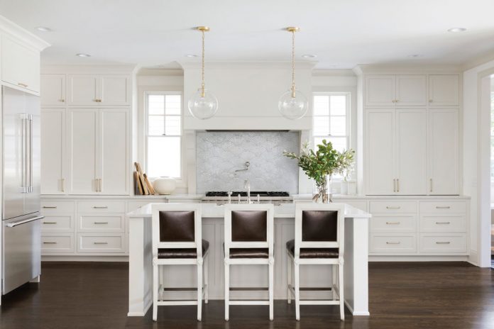 A kitchen in a home on Midwest Home's 2018 Luxury Home Tour that features a center island with seating, all white cabinetry, and a dark wood floor.