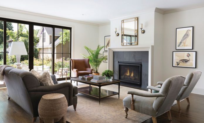 The living room in a home on Midwest Home's 2018 Luxury Home Tour that shows plenty of seating around a table with a plant on it, all next to a fireplace with a mirror hung above it.