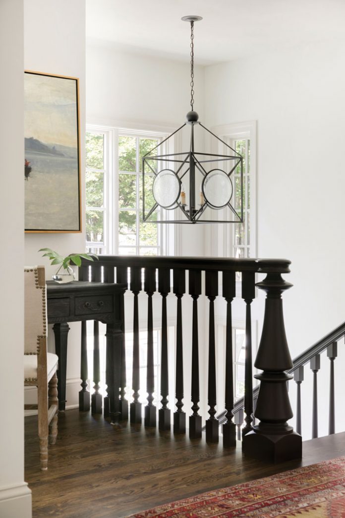 The top of a stairwell in a home on Midwest Home's 2018 Luxury Home Tour that shows a dark wood railing, and chandelier hanging over it.