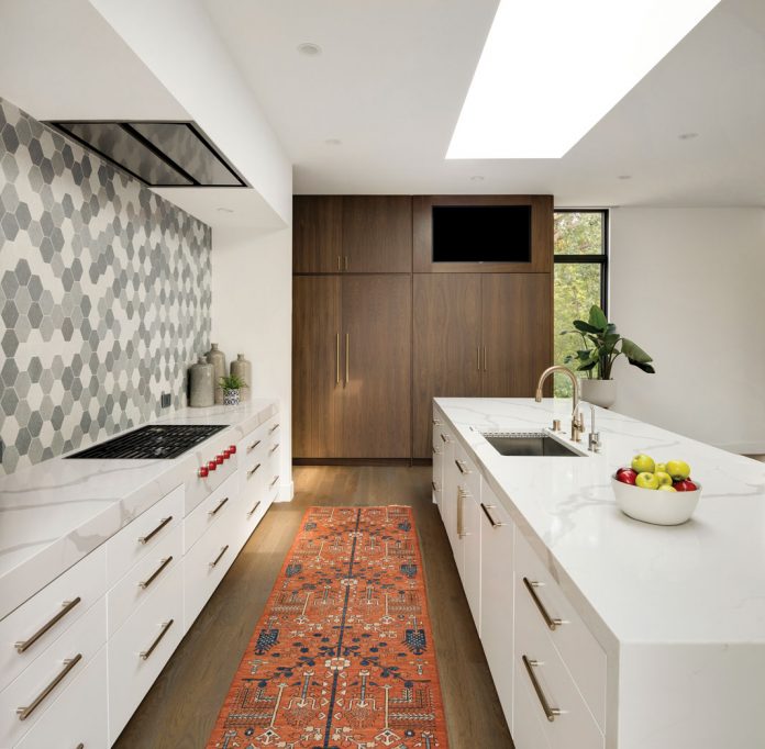 A kitchen in a home on Midwest Home's 2018 Luxury Home Tour that features white cabinetry, backsplash, and rug.