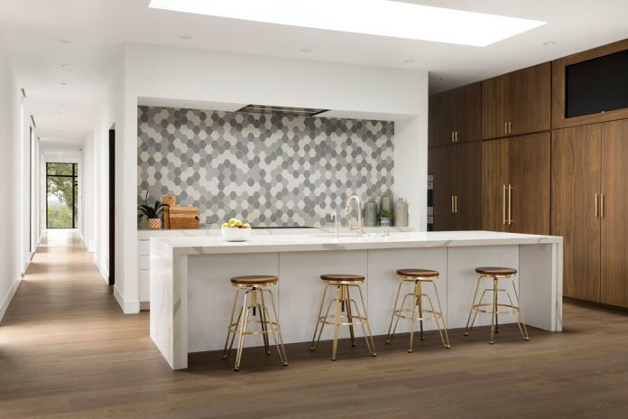 A kitchen in a home on Midwest Home's 2018 Luxury Home Tour that shows a white center island with seating, light wood flooring, and patterned backsplash.