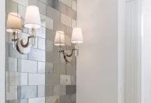 A bathroom with mirrored tiles, white sink and wall sconce light.