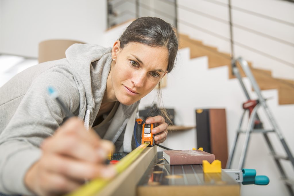 Woman measure 2-by-4 with tape measure.