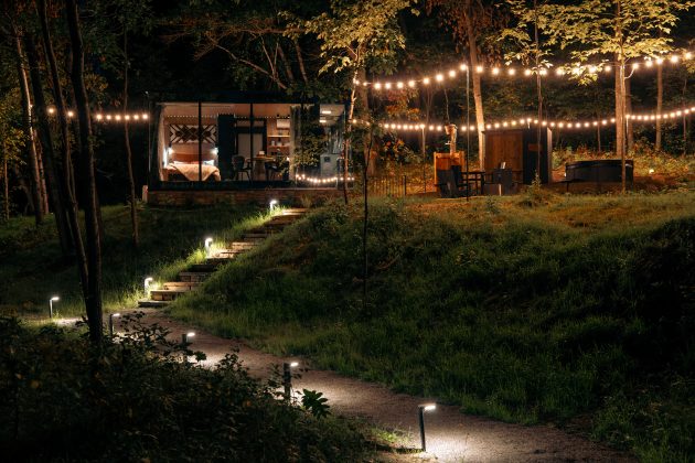 Wide shot of mirror cabin at nighttime with guiding lights leading up to the lot