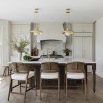 Enduring Elegance: A Timeless and Functional Kitchen Remodel Packed with custom cabinetry, the kitchen is the heart of the home. The warm oak island, accented by Ormandy pendant lights from Rejuvenation, anchors the space and provides contrast with the walls and millwork, painted in Benjamin Moore’s creamy Swiss Coffee shade.