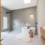 Large, minimalist bathroom with gray tiling, walk-in-shower, and freestanding bathtub.