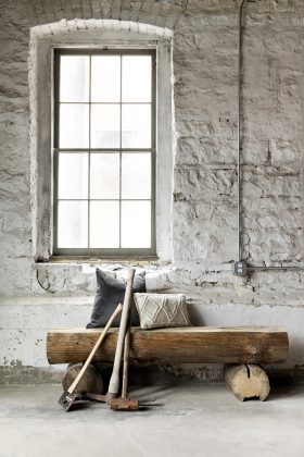A log bench beneath a window with axes leaning on it.