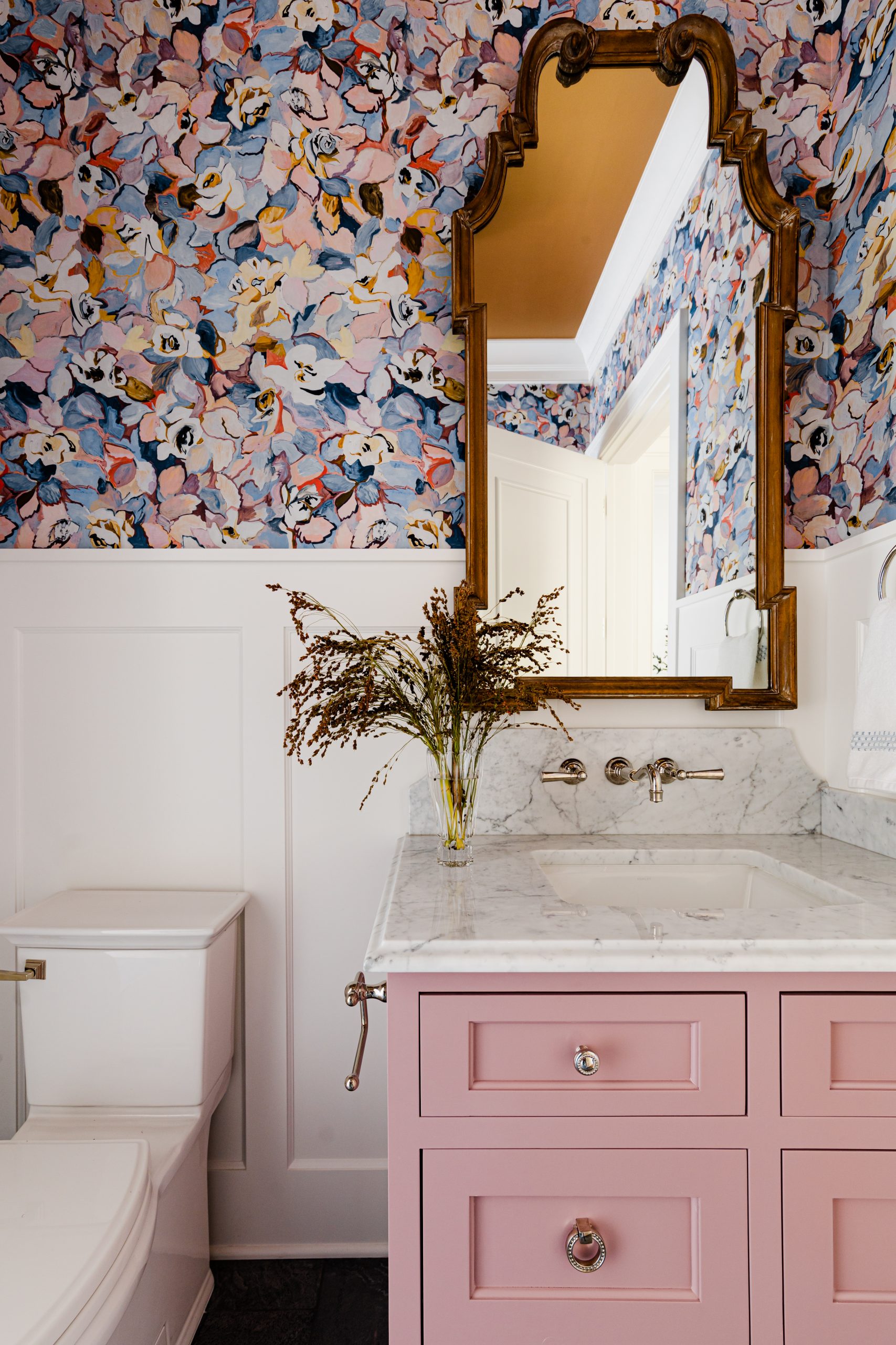 A bold abstract floral wallpaper and a custom, soft pink vanity add personality to this powder room from Chirigos Designs and Mark D. Williams Custom Homes.