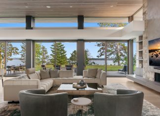 The great room is a focal point of the home and provides easy flow into the kitchen and adjacent four-season porch. Sage-blue, hand-tied Tibetan rugs complement the wood flooring, ceiling, and natural stone fireplace.