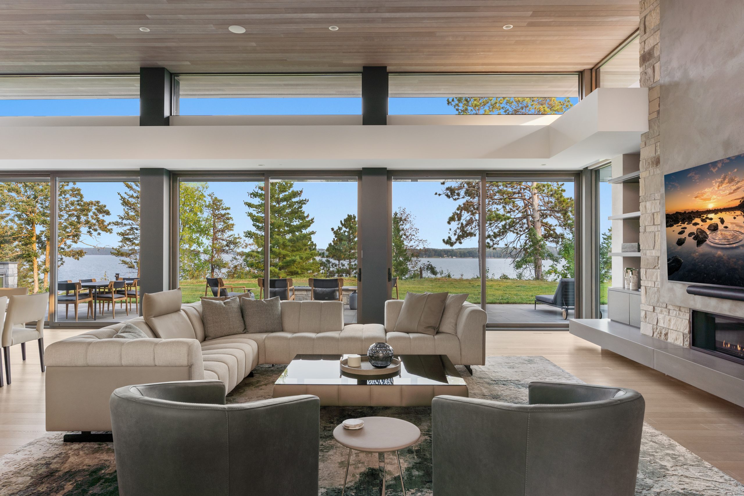 The great room is a focal point of the home and provides easy flow into the kitchen and adjacent four-season porch. Sage-blue, hand-tied Tibetan rugs complement the wood flooring, ceiling, and natural stone fireplace.