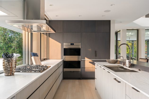 Cabinetry in the kitchen combines light-finished rift oak on the base cabinets with a darker tone on full-height elements, adding depth and balance. Bronze metal hardware and lighting introduce warmth.