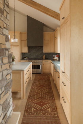 The kitchen features a spacious island distinguished by its chunky rounded legs, as well as a mix of metals including bronze cabinetry hardware and brushed brass light fixtures.