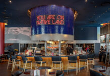 Indígena by Owamni interior with "You Are On Native Land" sign above the central bar. August 19, 2026