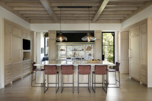 The kitchen blends quartzite surfaces with light-toned wood, and its wood beam ceiling creates a more intimate space off the grand, vaulted great room. Light fixtures above the island echo the home&rsquo;s organic yet refined sensibility.