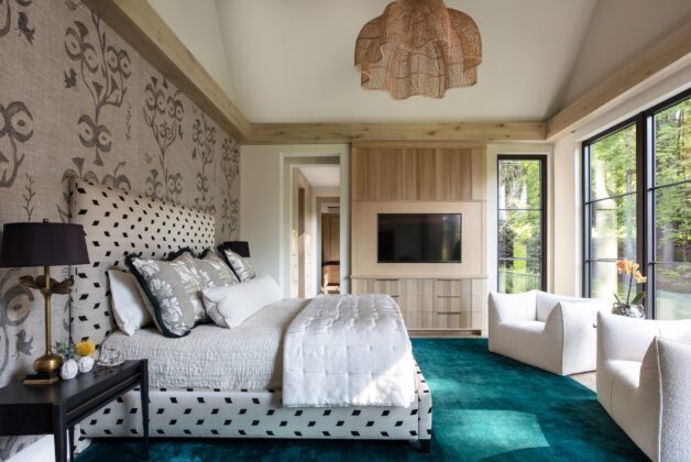 Floor-to-ceiling windows throughout the home, including in the primary bedroom, let in plenty of natural light and draw the eye outside to the woods and rolling hills that surround the estate. Touches of deep, jewel-toned color&mdash;like the bedroom&rsquo;s carpet&mdash; add richness and texture while pleasantly contrasting with the earth tones of the walls and woodwork.