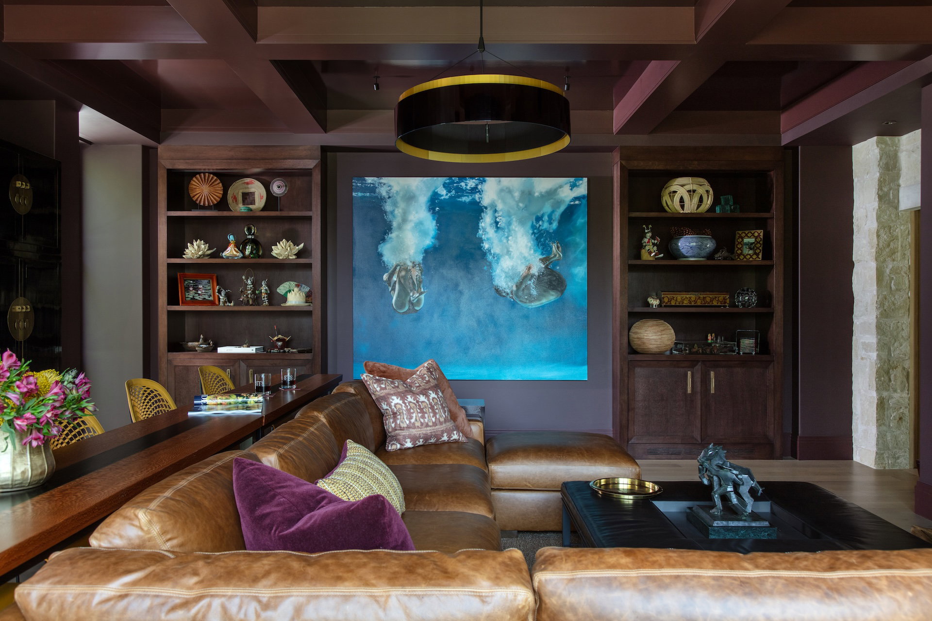 The cozy lounge is designed for family use and keeps the television separate from the main entertaining spaces. Rich merlot drenches both the walls and the glossy enamel ceiling, accented by an inviting leather sectional and mustard-yellow counter stools.